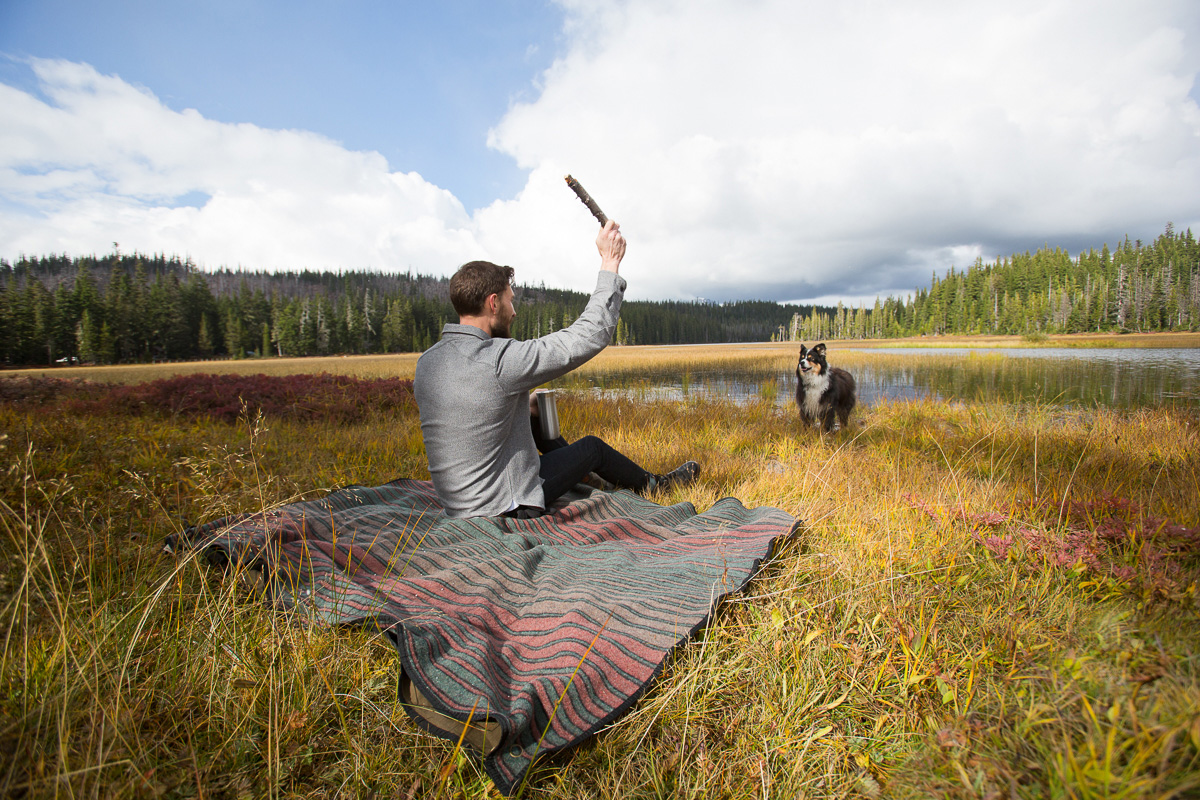 Man on blanket throwing a stick for dog, austrailian shepard, at an  Oregon mountain lake