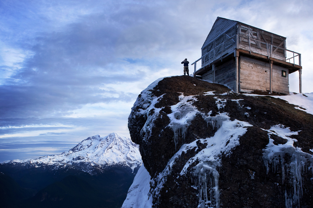 A man standing on an ice encrusted rock looking at Mt. Rainer form the high rocks lookout .